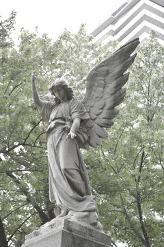 Vintage sad angel on a cemetery against the trees and leaves background. Holy angel.