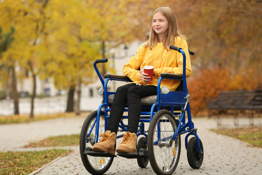 Little girl in wheelchair with cup of coffee outdoors