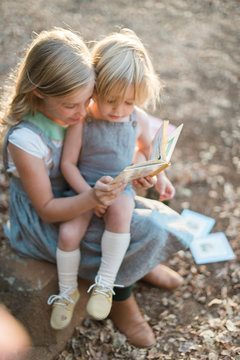 Young Girl and Boy Sit Reading Stories Outdoors