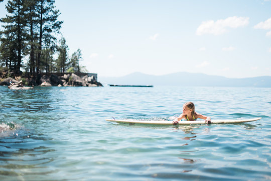 Young Girl Resting on Surfboard in Lake