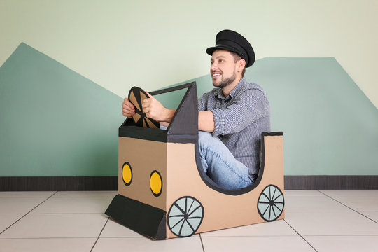 Young man dreaming of buying own auto while playing with cardboard car indoors