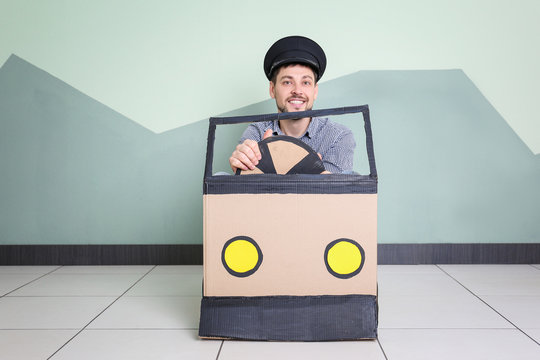 Young man dreaming of buying own auto while playing with cardboard car indoors