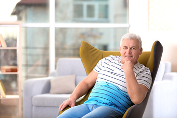 Handsome mature man sitting in comfortable armchair indoors