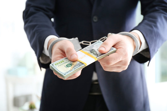 Businessman in handcuffs holding bribe on blurred background