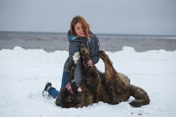 Happy woman playing with her dog on winter sea beach