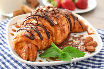 Yummy croissant with chocolate and caramel toppings on plate