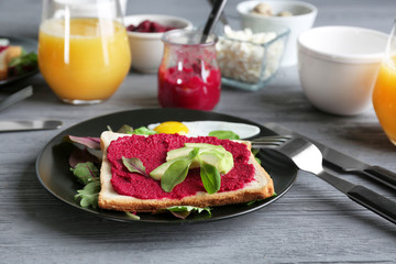 Plate with toast, beet paste and avocado on wooden table