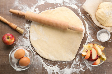 Raw dough and ingredients for apple pie on table
