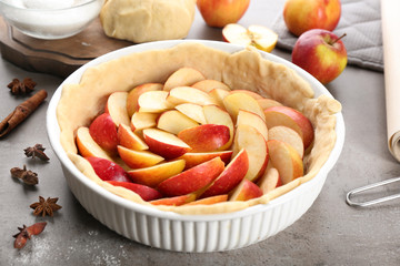 Raw dough with apples in baking dish on table