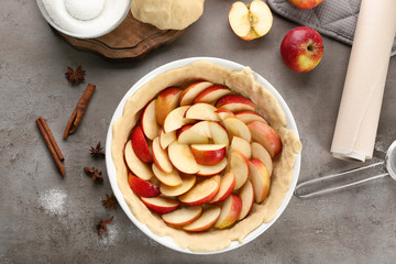 Raw dough with apples in baking dish on table