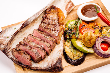 grilled beef steak on the bone with seasonings, fresh rosemary and grilled vegetables on a white background