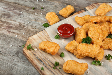 Wooden board with tasty chicken nuggets and sauce on table
