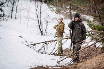 male and woman hunters ready to hunt, holding gun and walking in forest.