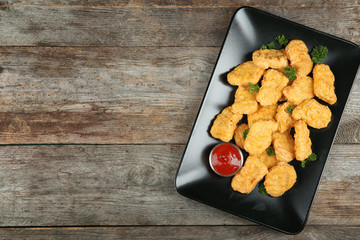 Plate with tasty chicken nuggets and sauce on table