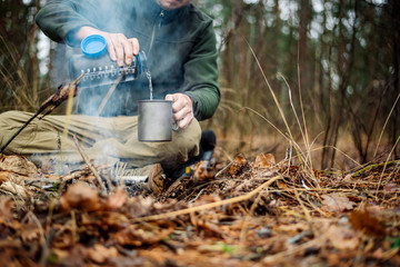 Obraz premium hunter pours water from a bottle into a metal mug. bushcraft, adventure, travel, tourism and camping concept.