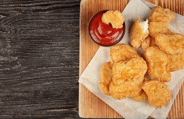 Wooden board with tasty chicken nuggets and sauce on table
