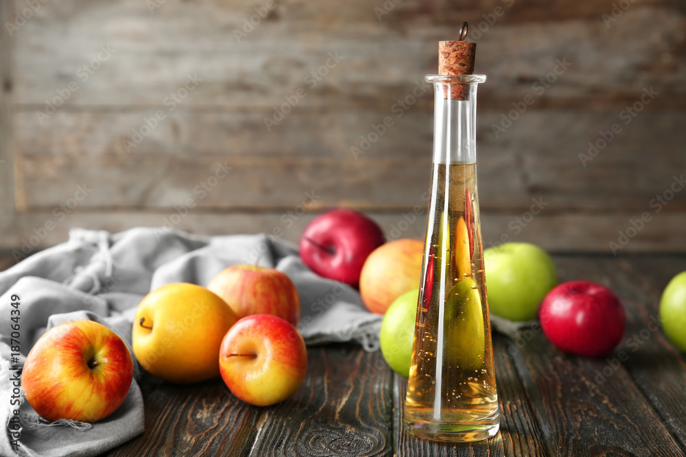 Wall mural Glass bottle with apple vinegar and fresh fruit on wooden table