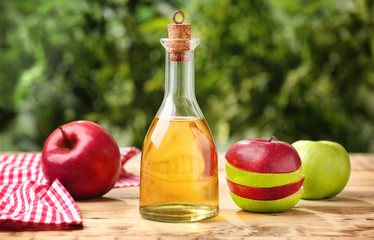 Glass bottle with apple vinegar and fresh fruit on wooden table