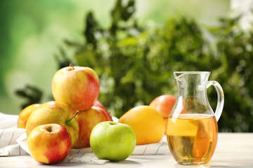 Glass jug with apple vinegar and fresh fruit on table