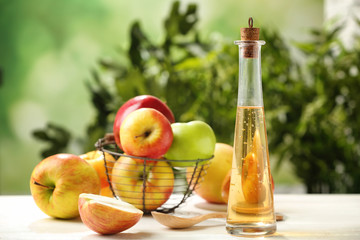 Glass bottle with apple vinegar and fresh fruit on table