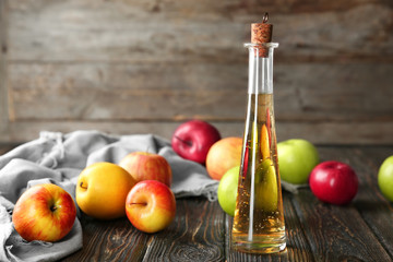 Glass bottle with apple vinegar and fresh fruit on wooden table