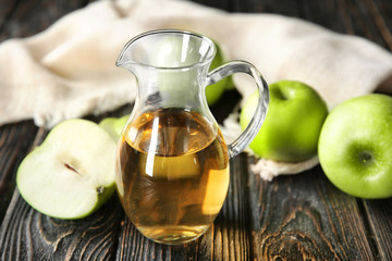 Glass jug with apple vinegar and fresh fruit on table