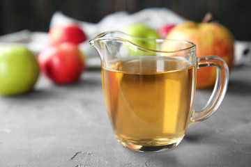 Glass jug with apple vinegar on table