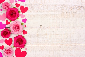 Valentines Day side border of red and pink paper hearts and roses against a rustic white wood background with copy space.