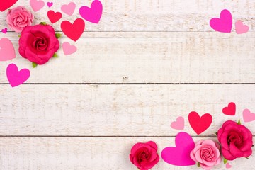 Valentines Day corner frame of red and pink paper hearts and roses against a rustic white wood background with copy space.