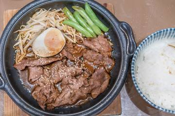 Korean Barbecued Pork in hot pan with egg, sprout and peas on side.