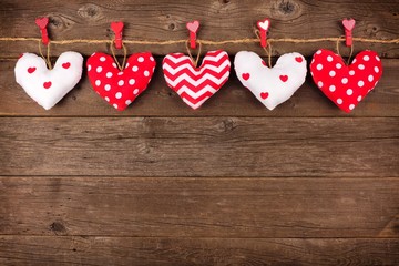 Fototapeta premium Valentines Day handmade, patterned cloth heart pillows hanging from line. Top border against a rustic old wood background.