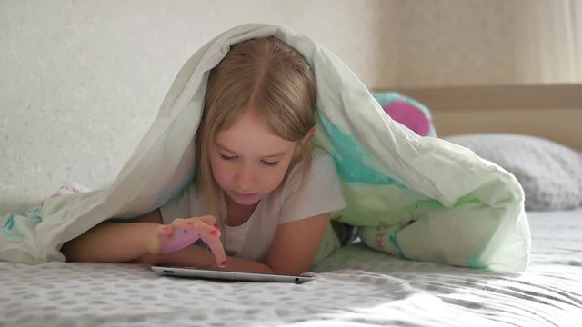 Teen girl using tablet pc on the bed under blanket