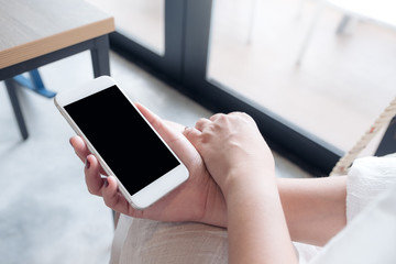Mockup image of a woman's hand holding white mobile phone with blank black desktop screen in loft cafe