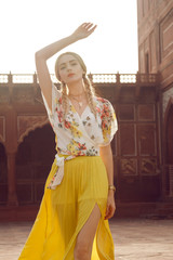 A beautiful young woman walking with a gorgeous bindi on her forehead. Long blonde hair is tangled in wonderful hairstyle. And she is dressed in a pretty shirt with floral print and yellow skirt.