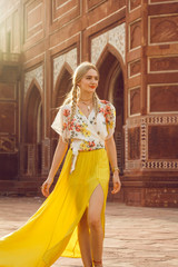 A beautiful young woman walking with a gorgeous bindi on her forehead. Long blonde hair is tangled in wonderful hairstyle. And she is dressed in a pretty shirt with floral print and yellow skirt.