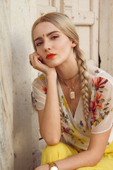 Fototapeta premium Close-up portrait of a beautiful young woman with a gorgeous bindi on her forehead. Long blonde hair is tangled. She is dressed in a pretty shirt with floral print and yellow skirt