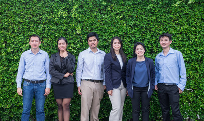 Team of Asian business man and woman looking at camera with smiling face outside office at green leaf wall.