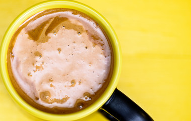 Coffee in a black mug on a yellow wooden background