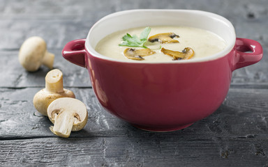 Cream soup of mushrooms with parsley on a wooden table. The decoration of raw mushrooms.