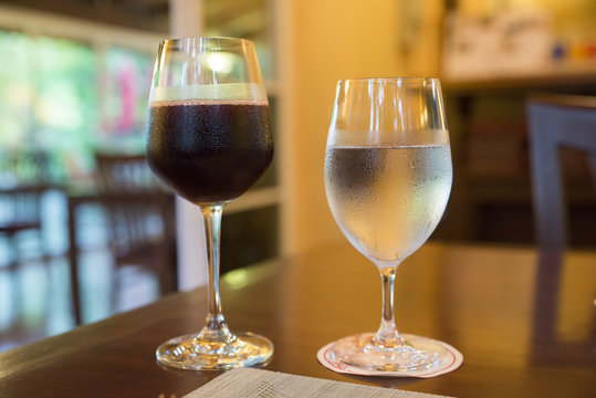 Glass of wine and a glass of cold water is placed on a wooden table in a restaurant at Valentine's Day of Couple of Love.