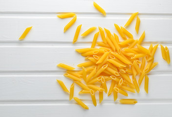 A lot of pasta is scattered on a white wooden table. The concept of eating.