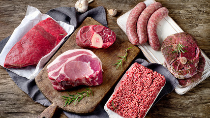 Different types of raw meat on dark wooden background.