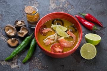 Bowl of green curry thai soup with some of its cooking ingredients over brown stone background, horizontal shot