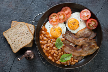 English breakfast served in a frying pan over cracked asphalt background, above view, horizontal shot