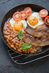 English breakfast with bacon, fried eggs, beans and tomatoes served in a metal pan, selective focus, vertical shot