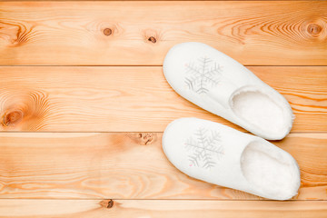 pair of white warm slippers with snowflakes view from above on a wooden floor