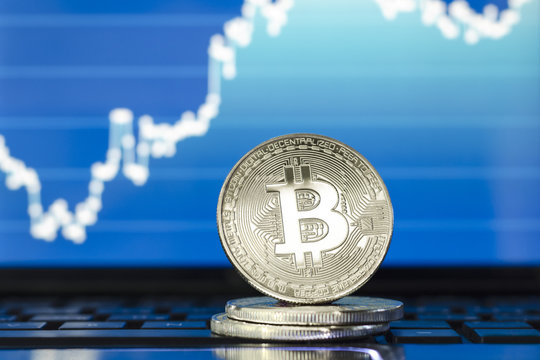 Bitcoin. Silver bitcoin coin on the laptop keyboard. Trading concept. Stock market graph.