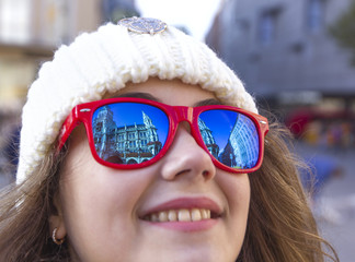 Beautiful smile of a young woman in blue red sunglasses, in which towers are reflected, the town hall of the old city of Munich, Germany