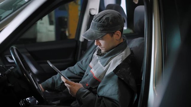 automotive technician is checking gearbox, is shifting gear and looking on a displays of car computer, sitting inside a car, enter data into a tablet