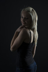 Fototapeta premium Beautiful blond woman in denim and black top in the dark with selective lighting